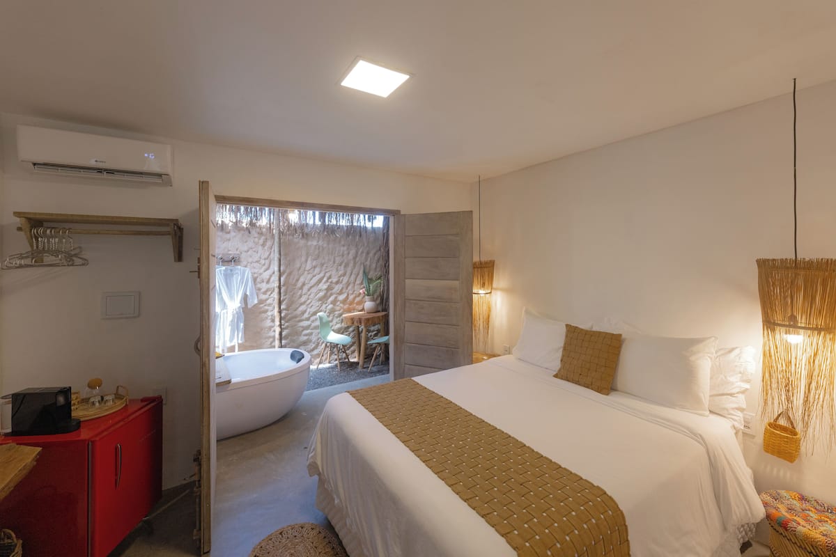 A bedroom with a large bed, a red cabinet, a bathroom with a bathtub, and a small table with chairs.