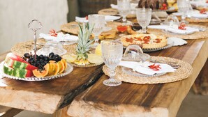 A long wooden table set with various dishes, glasses, and a wicker basket. - Pousada Villa Cacau (Porto Seguro)