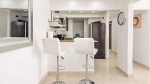 A modern kitchen with white cabinets, a stainless steel refrigerator, and two white bar stools.