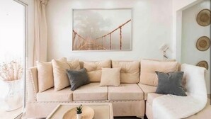 A beige sofa with multiple cushions, a small side table with a plant, and a framed picture of a bridge on the wall.