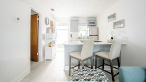 A modern kitchen with white cabinets, a stainless steel refrigerator, and a central island with two chairs. - Charming 1-Bedroom Oasis in the Heart of Downtown (New Port Richey)