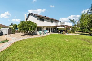 Ein zweistöckiges Haus mit überdachter Terrasse und Rasen.