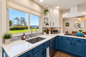 A modern kitchen with a large window, built-in cabinets, a stainless steel sink, and a blue countertop. - Spacious Family Retreat · Views · Hot Tub · BBQ · Sleeps 6-10 (San Diego)