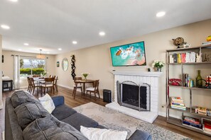 A modern living room with a fireplace, a dining area, and a bookshelf. - Spacious Family Retreat · Views · Hot Tub · BBQ · Sleeps 6-10 (San Diego)