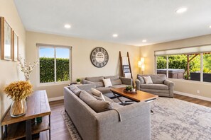 A spacious living room with a large sofa set, a coffee table, and a clock on the wall. - Spacious Family Retreat · Views · Hot Tub · BBQ · Sleeps 6-10 (San Diego)