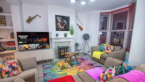 Un saló amb una xemeneia, sofàs, coixins de colors, una televisió que mostra 'Stranger Things' i un saxòfon a la paret.