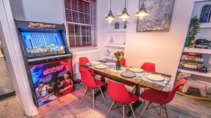 Zona de menjador amb taula de fusta, cadires vermelles, una màquina recreativa de Street Fighter II i una estanteria amb llibres i un joguet de peluix.