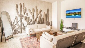 A living room with a large cactus wall mural, a white sofa, a coffee table, and a flat-screen TV on the wall.