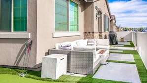 A patio with a white outdoor sofa, a grill, and a small garden area with artificial grass and stepping stones.