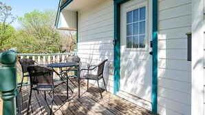 A covered patio with a table and chairs, a door with a window, and a white exterior with teal trim. - The Sunflower Cottage (San Marcos)