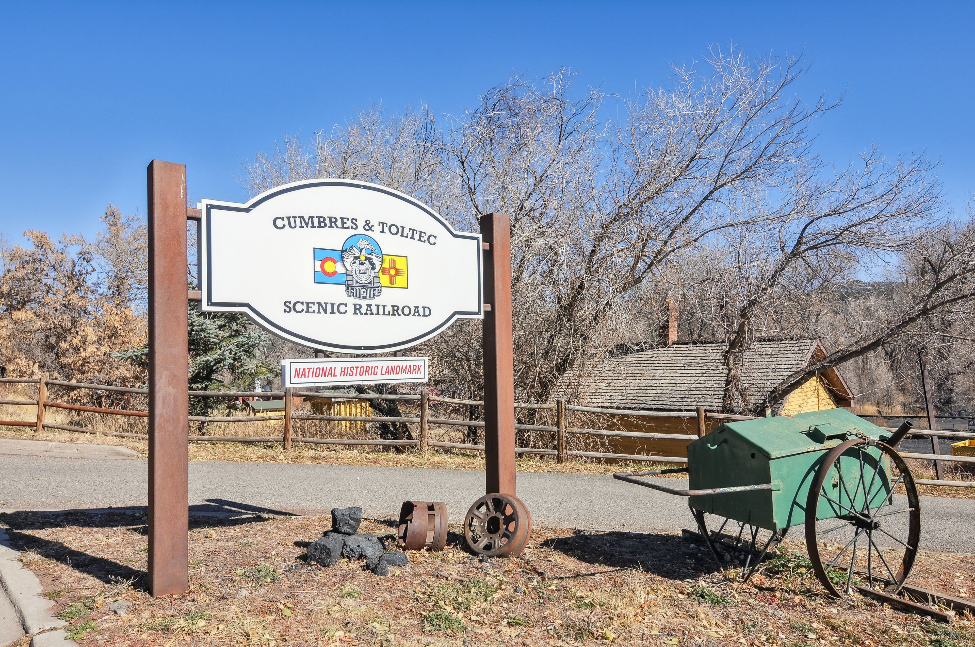 Une pancarte indiquant le chemin vers le Cumbres & Toltec Scenic Railroad, un site historique national, avec une clôture en bois et un wagon vert à l’arrière-plan.