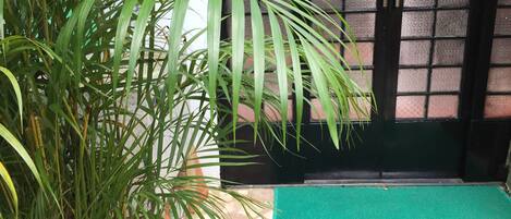 A green mat with "WELCOME" in gold letters, a potted plant, and a tiled floor.