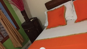 A hotel room with a neatly made bed, a wooden headboard, and a green wall with curtains. - Apartahotel Tierras Amazonicas (Leticia)
