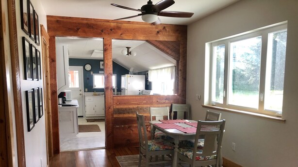 A dining area with a wooden table and chairs, a ceiling fan, and a view of a kitchen and living area through an open doorway.