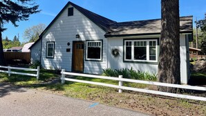 A white single-story house with a brown door, a small porch, and a white fence in front.