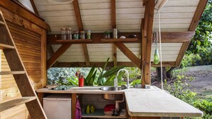 A rustic wooden kitchen with a built-in sink, shelves with jars, and a small refrigerator. - Villa Tiki a harmonious composition with a charming bungalow and private pool (Le Moule)