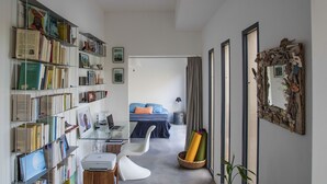 A modern living room with a glass coffee table, a white sofa, a bookshelf filled with books, a laptop, and a bed with blue bedding. - Villa Tiki a harmonious composition with a charming bungalow and private pool (Le Moule)