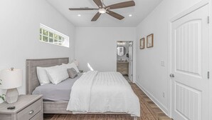 Ein Schlafzimmer mit Bett, Nachttisch, Lampe, Deckenventilator und einer Tür.