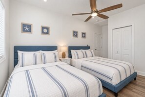 A bedroom with two beds, a ceiling fan, and nautical-themed wall art.