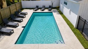 Ein rechteckiger Pool mit klarem, blauem Wasser, umgeben von einer Betonplattform. Sechs Liegestühle sind entlang des Poolrandes aufgereiht.