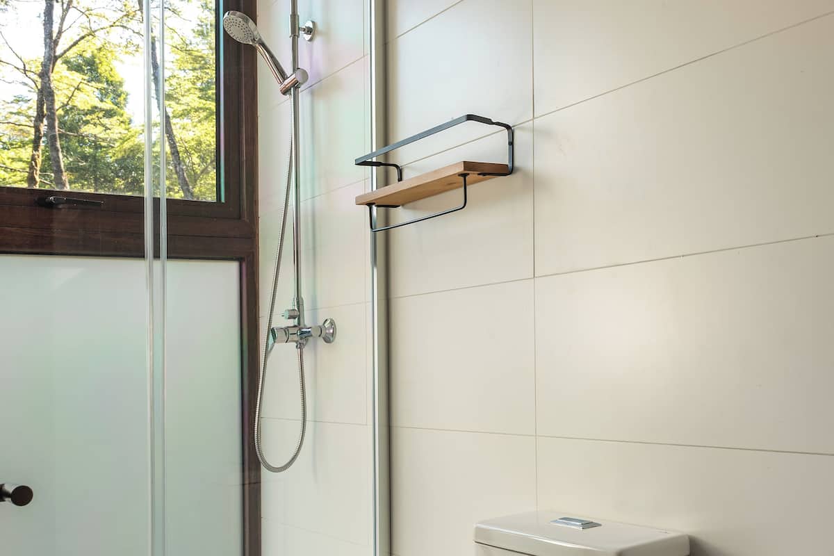 A modern bathroom with a glass shower enclosure, a toilet, and a wooden shelf.