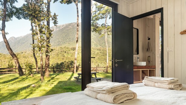 Un dormitorio con cama, toallas y vistas a una zona verde con árboles y montañas.