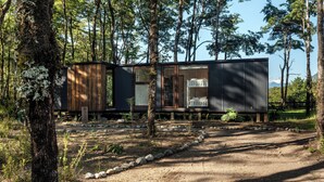 Una cabaña moderna con un amplio ventanal, rodeada de bosque.