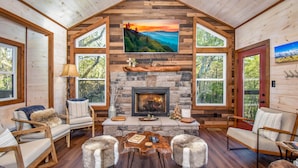 A cozy cabin interior with a stone fireplace, wooden walls, and large windows offering scenic views. - 3 King Beds 3.5 Bath Cabin-Hot Tub-Pool Table, Great Smoky Mountains (Sevierville)