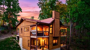 A two-story wooden cabin with a balcony, surrounded by trees. - 3 King Beds 3.5 Bath Cabin-Hot Tub-Pool Table, Great Smoky Mountains (Sevierville)