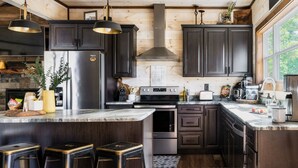 A modern kitchen with dark wood cabinets, stainless steel appliances, and a large island with bar stools. - 3 King Beds 3.5 Bath Cabin-Hot Tub-Pool Table, Great Smoky Mountains (Sevierville)