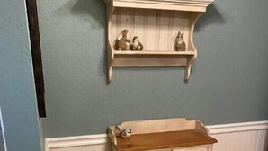 Una habitación con un armario de madera, una cesta de mimbre con toallas y un estante de pared con figuritas.