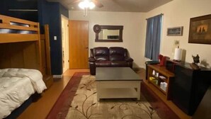Una habitación con una cama nido, un sofá, una mesita de centro, un ventilador de techo, un espejo y un televisor.