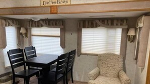 Interior compacto de una caravana con una mesa de comedor y sillas, un sillón acolchado y un cartel que dice "Count Your Blessings".