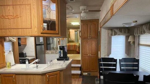 Cocina compacta para autocaravana con armarios de madera, cafetera y zona de comedor con mesa y sillas.