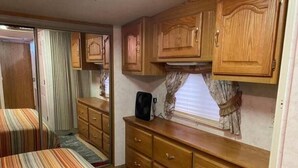 Interior compacto de una caravana con una cama a rayas, armarios de madera y una pequeña zona de kitchenette.