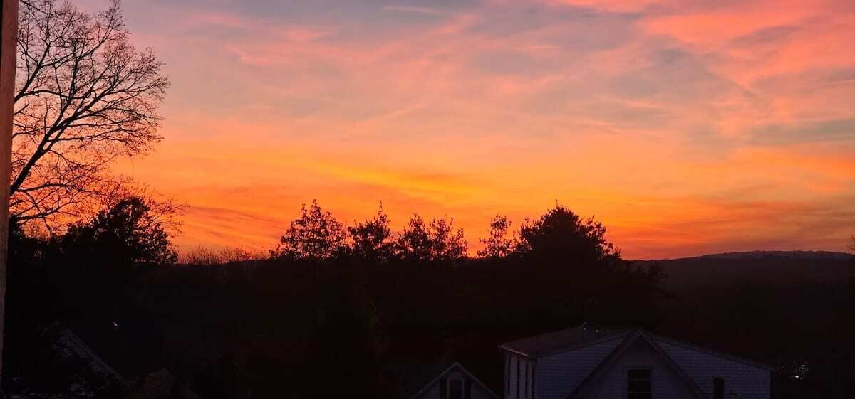 A sunset view with silhouettes of trees and a house.