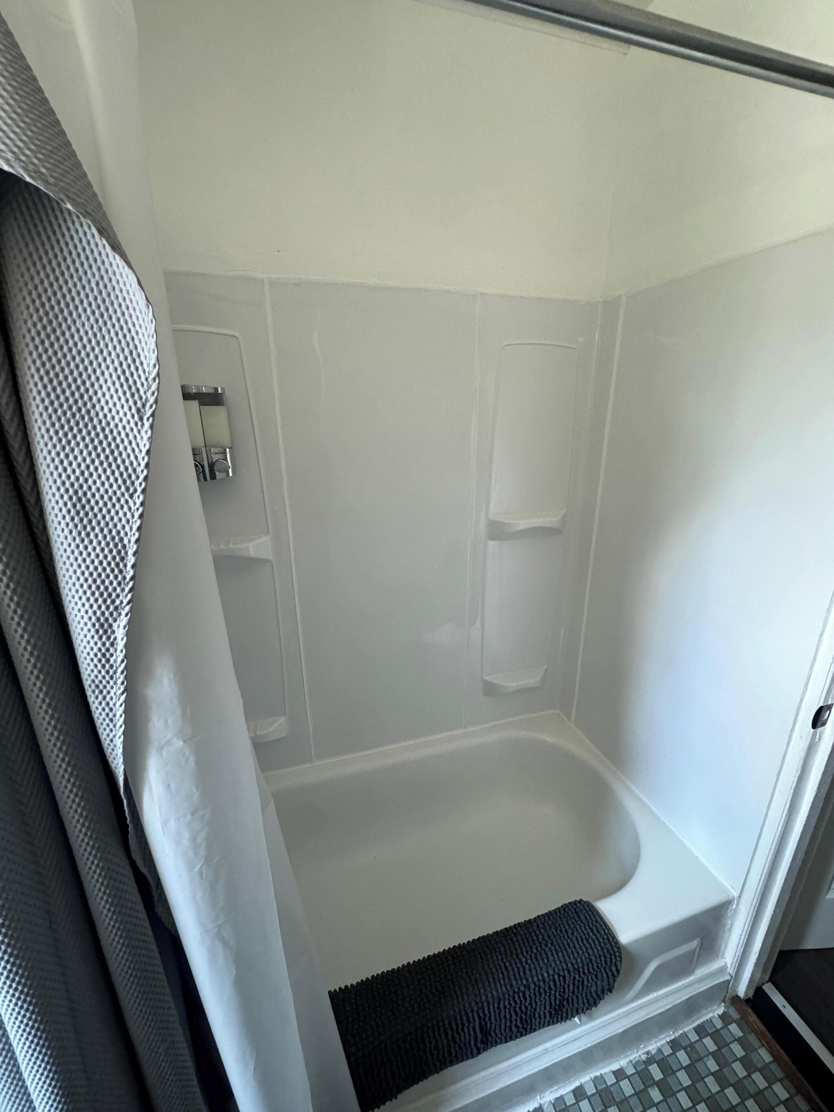 A small, enclosed shower area with a bathtub, a shower curtain, and a tiled floor.