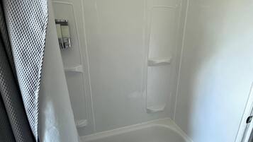 A small, enclosed shower area with a bathtub, a shower curtain, and a tiled floor.