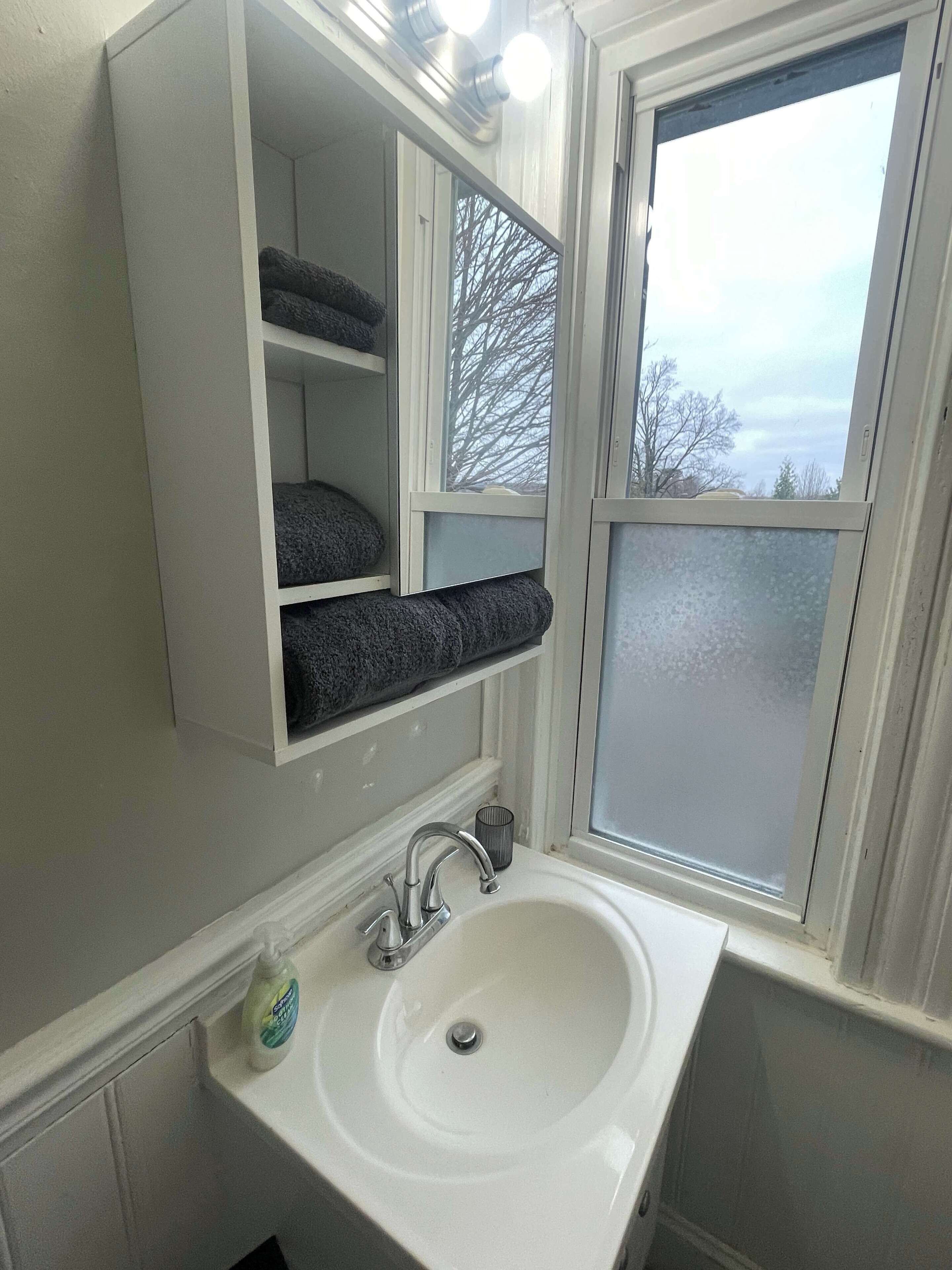 A bathroom with a white sink, a mirror, and a window.