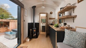 Une cuisine compacte dotée d’un poêle à bois central, de meubles en bois et d’un banc intégré avec un coussin.