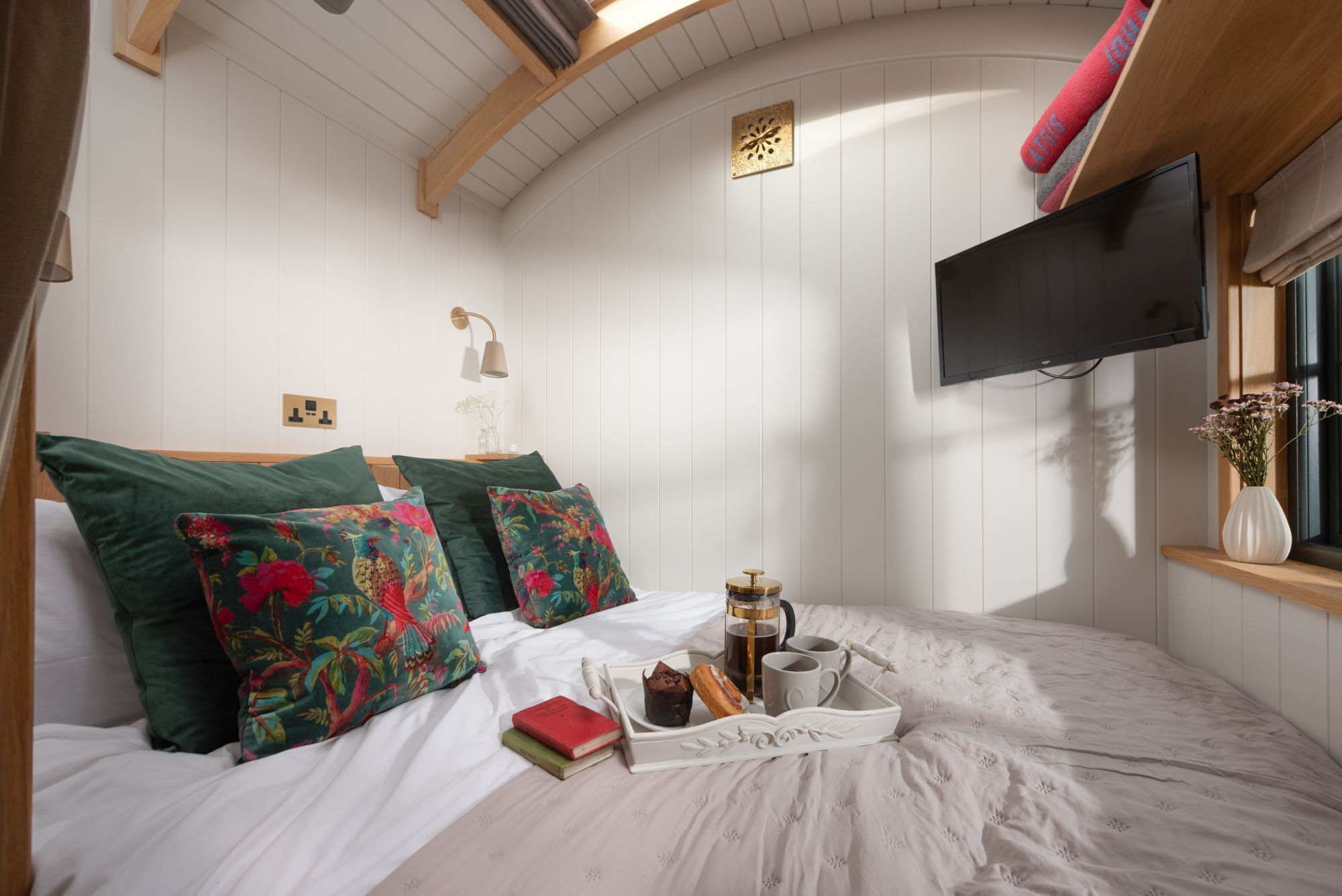 A cozy bedroom with a bed, pillows, a bedside table with a lamp, a TV, and a window with a view.