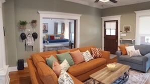 Un salon avec un canapé d’angle, une table basse et un canapé gris. On y trouve un ventilateur de plafond, une décoration murale représentant un vélo et une porte avec une fenêtre.
