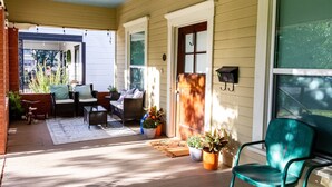 Une véranda couverte, aménagée avec des meubles d’extérieur, des plantes en pot et une porte donnant sur la maison.