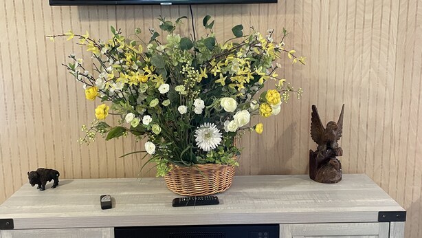 A fireplace with a fire, a television mounted on the wall, a decorative basket with flowers, and a small figurine on a wooden cabinet. - Meadow Farm-View Getaway (Sparta)