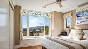 A bedroom with a large window, a bed, a ceiling fan, and a view of the outdoors.