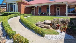 A two-story brick house with a red roof, a curved driveway, and a landscaped front yard with rocks and shrubs.