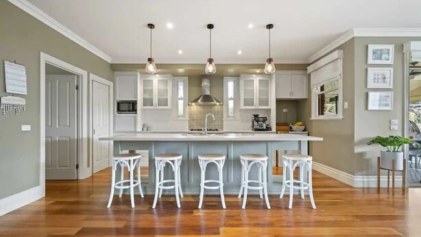 A modern kitchen with white cabinetry, a central island with bar stools, pendant lighting, and a view of the adjacent living area.