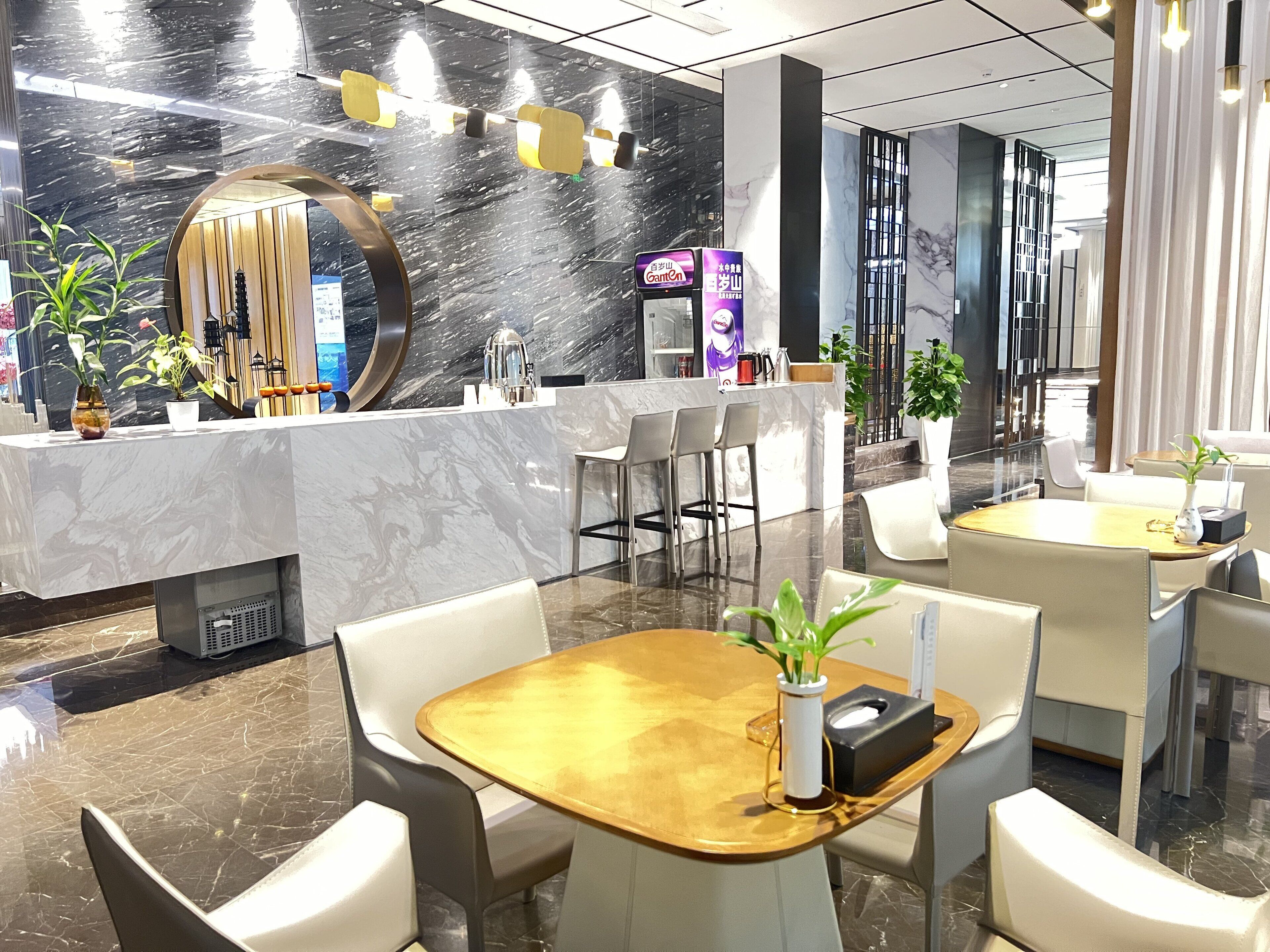 A modern hotel lobby with marble walls, a reception desk, seating area, and a large mirror.