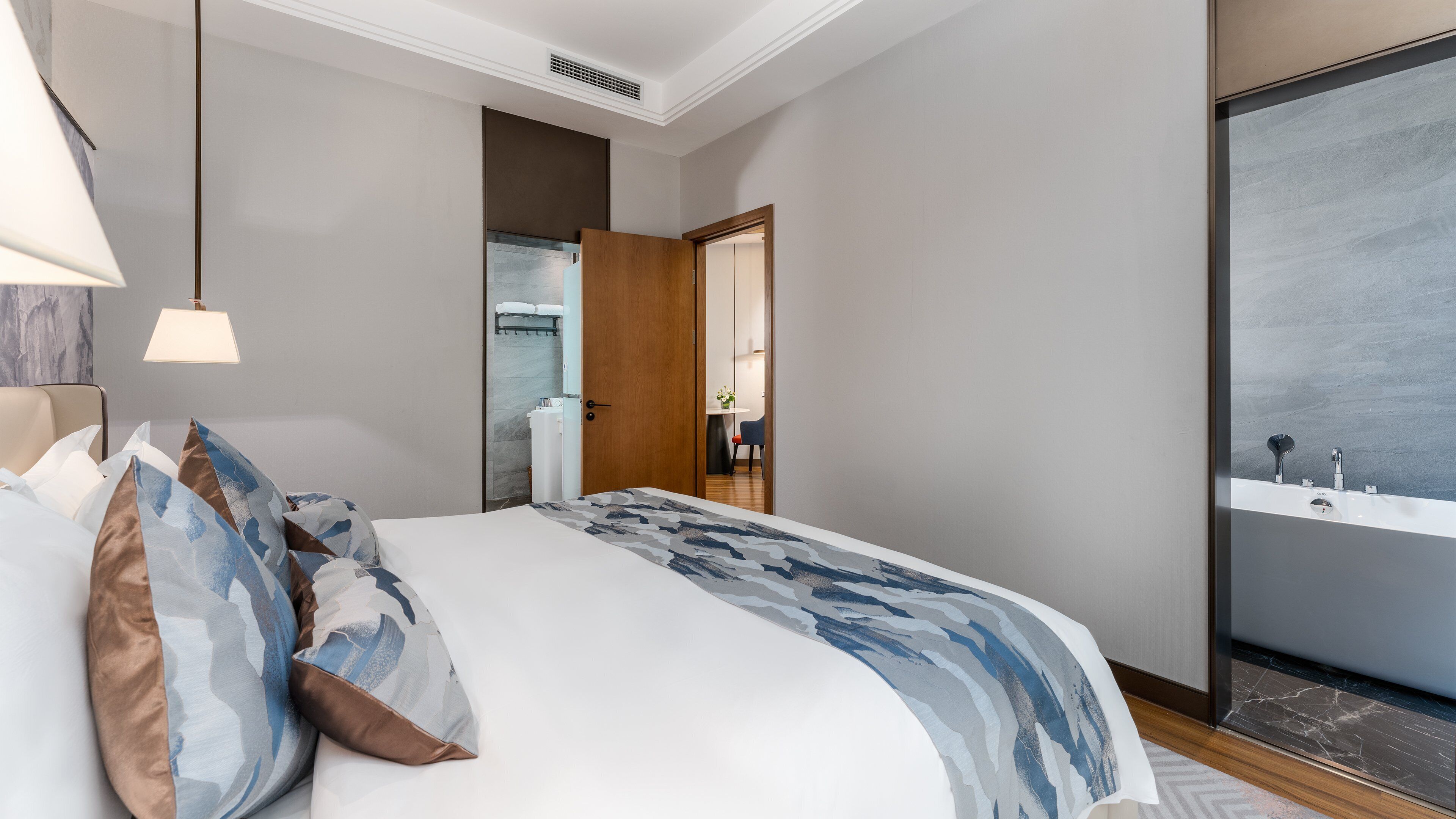 Une chambre d’hôtel moderne avec un grand lit, une table de chevet, une lampe et une vue sur la salle de bain.