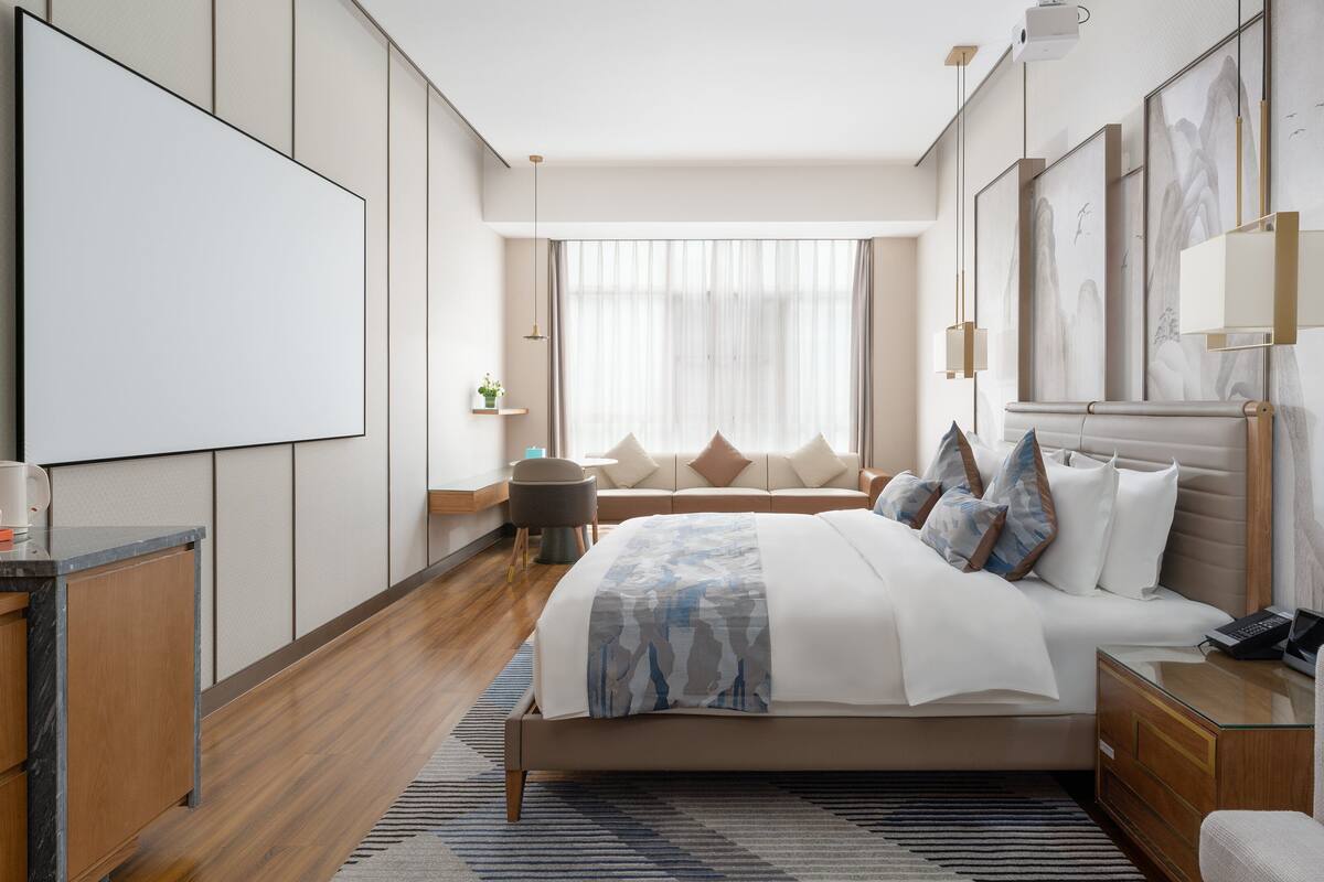 A modern hotel room with a large bed, a desk, and a seating area.